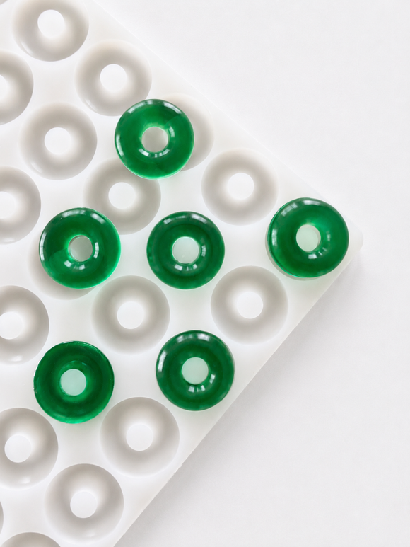 Angled view of the 3.4mL peach ring gummy mold with 108 cavities and translucent emerald green peach ring gummies