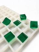 Side-angle view of a 6mL square gummy mold with 165 cavities and translucent emerald green square gummies on a white background