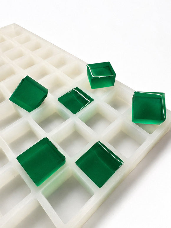 Side-angle view of a 6mL square gummy mold with 165 cavities and translucent emerald green square gummies on a white background
